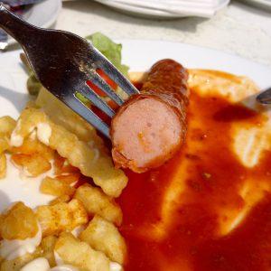 Wurst im Querschnitt auf der Gabel, Teller mit Soße und Pommes im Hintergrund - Walsrode Restaurants