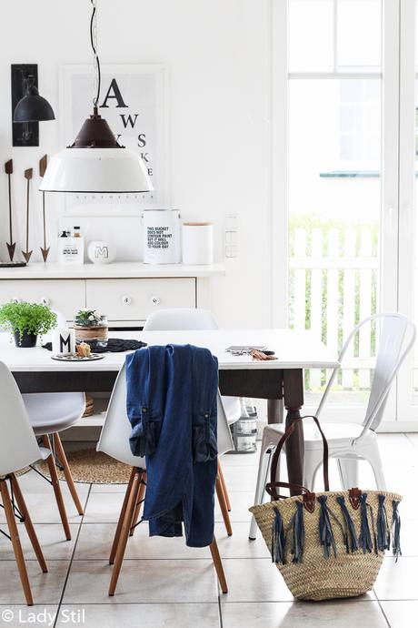 Ibizakorbtasche mit Jeans-Tasseln steht auf dem Küchenboden neben dem weißen Tisch und weißen Stühlen, über der Stuhllehne liegt eine Jeansjacke
