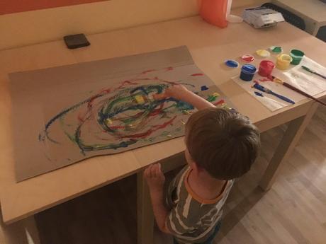 Beschäftigungsideen für Kleinkinder: Kind malt mit Fingerfarbe und Pinsel einen großen Karton bunt an.