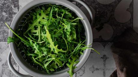 Welche Kräuter passen zusammen? Ein Sieb voller Rucola steht auf einem Fliesenboden