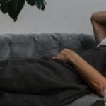 Krankenstand auf Rekordhoch: Wie du als Arbeitgeber gegensteuern kannst Ein Mann liegt krank auf einer Couch - Sinnbild für den hohen Krankenstand in Deutschland