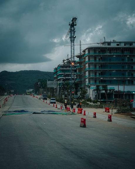 Nusantara 2025: Unsere Reise in Indonesiens neue Hauptstadt In einer verlassenen Straße in Nusantara sind Hochhäuser und ein Kran inmitten einer Baustelle zu sehen. Unter einem bewölkten Himmel säumen Verkehrsleitkegel den Weg.