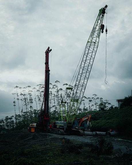 Nusantara 2025: Unsere Reise in Indonesiens neue Hauptstadt Die Nusantara-Baustelle mit großen Kränen und Maschinen, eingebettet zwischen hohen Bäumen unter einem bewölkten Himmel, zeigt die harmonische Verbindung von Natur und Fortschritt.