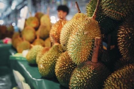 Die 8 wichtigsten Sehenswürdigkeiten in Kuala Lumpur Auf einem Markttisch ausgestellte Duriansorten, im Hintergrund eine Person in einer geschäftigen Umgebung.
