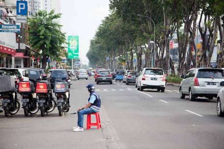 Vogelbeobachtung – Die besten Spots weltweit Straße in Jakarta. Ein MAnnn sitzt auf der Fahrbahn mit einem orangen Plastikhocker