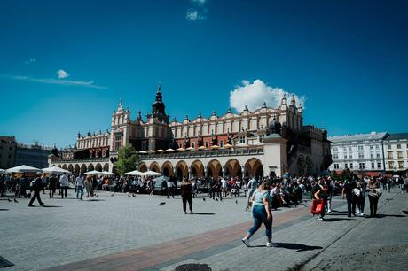 Die 10 besten Sehenswürdigkeiten in Krakau Menschenmengen versammeln sich auf einem sonnigen Platz vor einem historischen Gebäude mit Bögen und einem zentralen Turm.