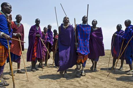 Digitaler Nomade in Tansania: Arbeiten zwischen Serengeti und Sansibar Eine Gruppe von Massai in farbenfroher traditioneller Kleidung steht im Freien und hält Holzstäbe.