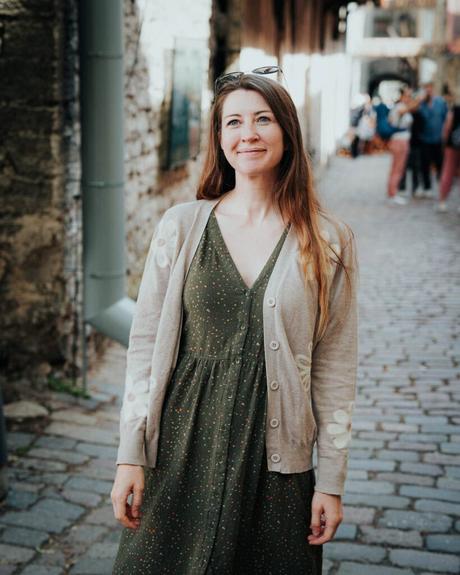 Tallinn: Die 10 besten Sehenswürdigkeiten Eine Frau in einem grünen Kleid und einer beigen Strickjacke steht lächelnd auf einer Kopfsteinpflasterstraße in Tallinn.