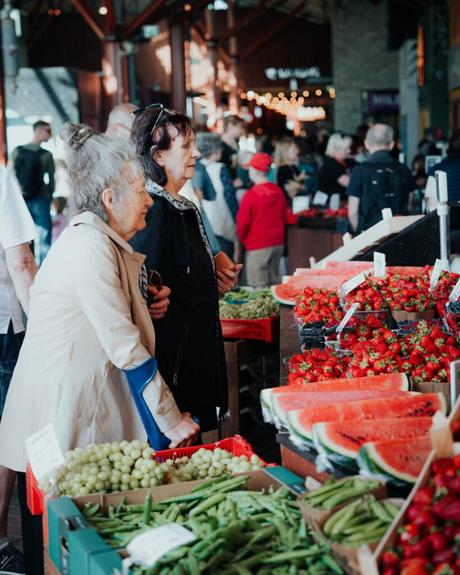 Tallinn: Die 10 besten Sehenswürdigkeiten Zwei Frauen stehen an einem Marktstand in Tallinn, umgeben von Erdbeeren, Wassermelonen, Weintrauben und anderen frischen Produkten.
