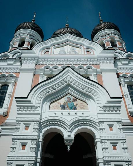 Tallinn: Die 10 besten Sehenswürdigkeiten Weiße, reich verzierte russisch-orthodoxe Kirche mit Kuppeln und religiösen Ikonen, aus einem niedrigen Winkel vor dem blauen Himmel in Tallinn gesehen.