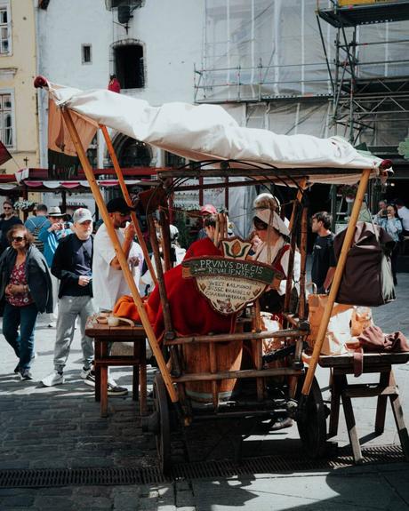 Tallinn: Die 10 besten Sehenswürdigkeiten Auf einem mittelalterlich angehauchten Straßenkarren in Tallinn sind kostümierte Menschen zu sehen, die auf einem belebten Stadtplatz von Passanten umgeben sind.