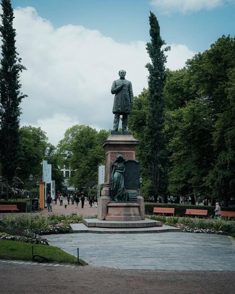 Helsinki: Die 10 besten Sehenswürdigkeiten Statue eines Mannes auf einem Sockel in einem Park in Helsinki, umgeben von üppigem Grün und Spaziergängern.