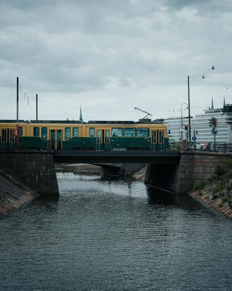 Helsinki: Die 10 besten Sehenswürdigkeiten Eine gelbe Straßenbahn überquert eine Brücke über einen Kanal unter einem bewölkten Himmel in der Stadtlandschaft von Helsinki.