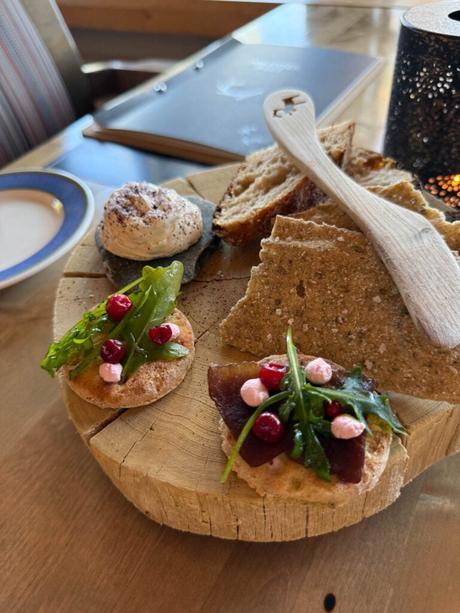 Im Bann des Mitternachtslichts: Ein Abenteuer in Finnisch-Lappland Handwerklich hergestelltes Brot, Knäckebrot, geschlagene Butter und Vorspeisen mit Grünzeug und Beeren auf einem rustikalen Holzbrett.
