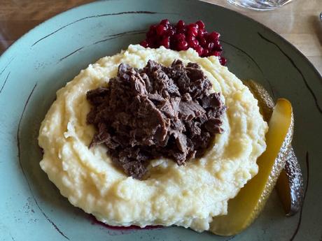 Im Bann des Mitternachtslichts: Ein Abenteuer in Finnisch-Lappland Kartoffelpüree mit geraspeltem Fleisch, serviert mit Essiggurken und Preiselbeeren auf einem grünen Teller.