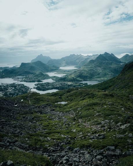 Svolvær und die Teufelspforte Eine malerische Aussicht auf üppig grüne Berge und Seen unter einem bewölkten Himmel.