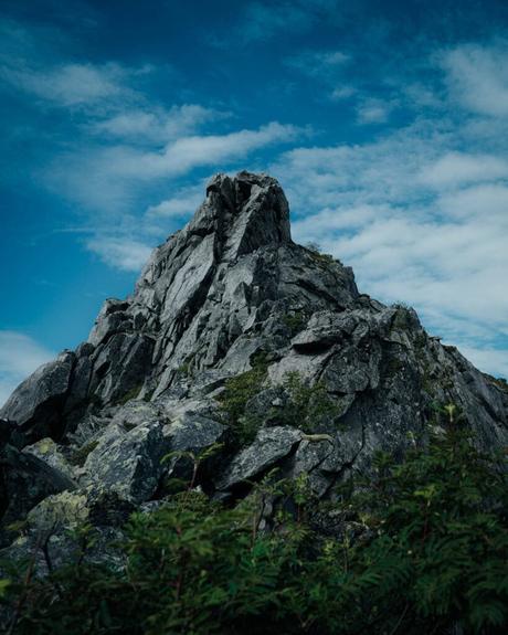 Svolvær und die Teufelspforte Zerklüfteter felsiger Berggipfel mit vereinzeltem Grün unter einem teilweise bewölkten blauen Himmel.