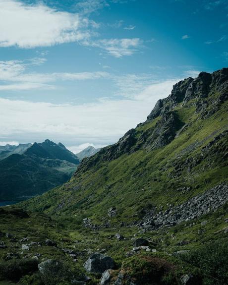 Svolvær und die Teufelspforte Ein üppig grüner Berghang mit felsigem Gelände unter einem teilweise bewölkten blauen Himmel.