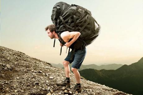 Ein Mann, trägt einen viel zu großen, falsch gepackten und zu schweren Rucksack auf seinen Rücken einen Berg hinauf!