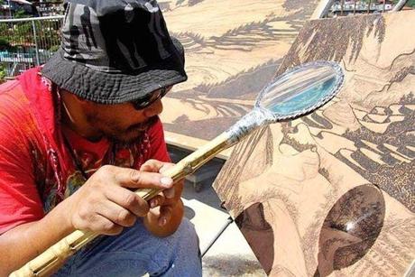 Künstler brennt mit Lupe und Sonne Bilder in Holz