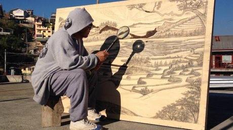Künstler brennt mit Lupe und Sonne Bilder in Holz