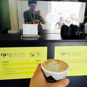 Cappuccino mit Baristaart vor der Maschine und rp15 Schildern