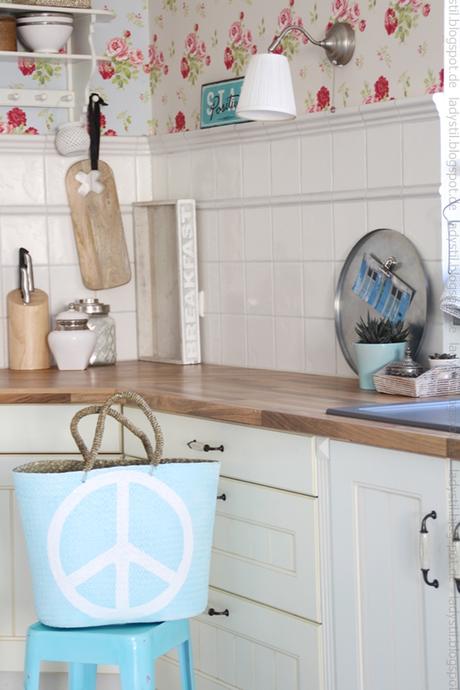 Blick auf die Küchenzeile mit Deko in Holz, Türkis und weiß davor steht der hellblaue Korb mit Peacezeichen