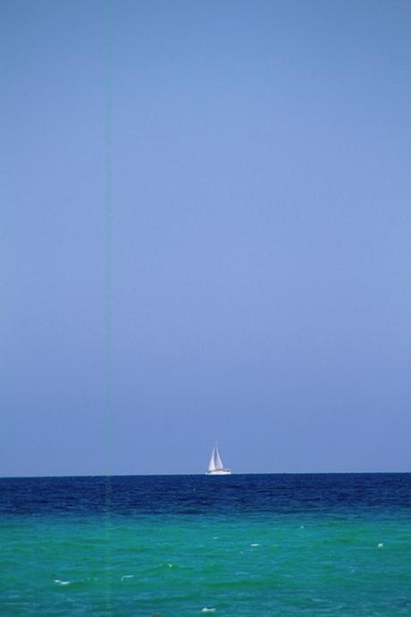 Blick übers türkisfarbene Meer mit weißem Segelboot und strahlendblauem Himmel