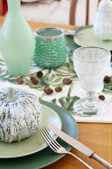 Herbstliche Tischdeko mit grüner Kürbisdekoration und kleinen Tannenzapfen sowie grüner Vase und Windlicht