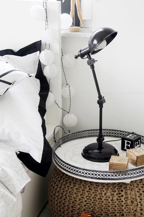 Interior Schlafzimmer in weiß schwarz Holz mit Pouf als Nachttisch und Industrialstyle Lampe