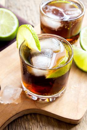 Rum and cola Cuba Libre drink with lime and ice on rustic wooden table