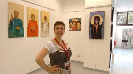 Künstlerin Olga David mit ihren Bildern im Hintergrund