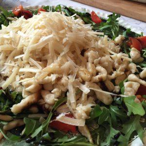 Parmesanspätzle auf Rucolasalat mit Pinienkernen und Cherrytomaten - Nahaufnahme