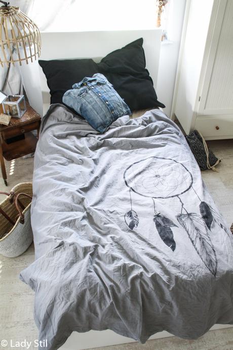 Einblick Schlafzimmer mit grauer Bettwäsche, auf der ein selbstgemalter Traumfänger abgebildet ist