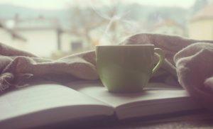 Ein aufgeschlagenes Buch auf einer Fensterbank, darauf steht eine dampfende Tasse Tee