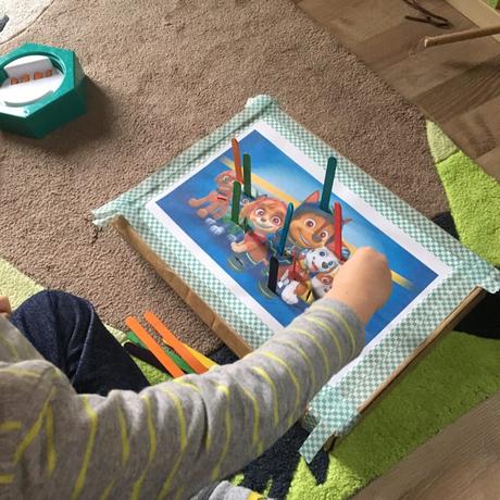 Kind spielt mit selbstgemachten Steckspiel. Bunte Eisstiele werden in die bunte Motiv zur passenden Farben rein gesteckt.