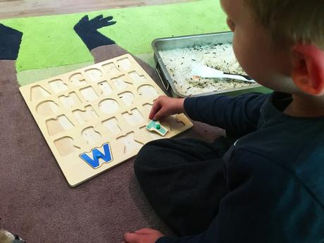 Kind spielt mit Buchstaben Puzzle. Die Buchstaben sind in einen flachen Gefäß unter Reis versteckt. Dieses Spiel ist einer der ersten Schritte zum Buchstaben und schließlich zum Lesen lernen.