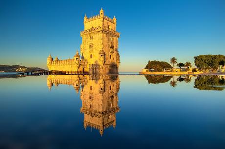 Wassertemperatur Lissabon: Torre de Belém spiegelt sich im stillen Wasser bei wolkenlosem Himmel.