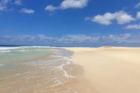 Wassertemperatur Kapverden: Verlassener, vegetationsloser Sandstrand mit flachem, grünlichen Wasser unter blauem Himmel