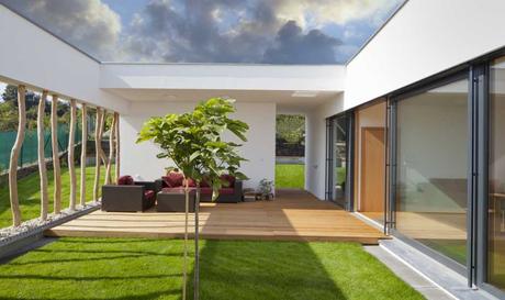 Eine Terrassenüberdachung aus Glas rahmt den Garten und die Sitzecke der Terrasse perfekt ab. Elemente aus Holz bringen einen natürlichen Look in die Modernität des Gartens. 