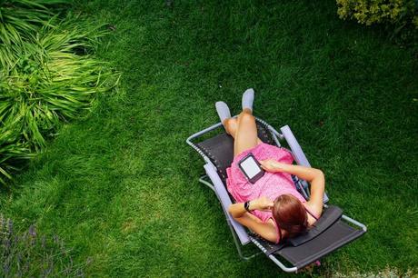 Liegestuhl im Garten, Frau sitzt darauf und liest ein eBook.