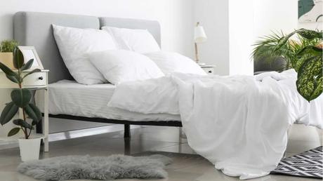 Bett mit weißer Bettdecke und Kissen außen rum Pflanzen