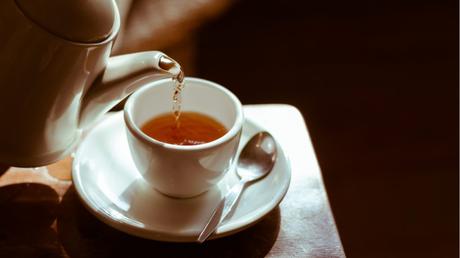 aus Teekanne wird Tee in eine Tasse gefüllt