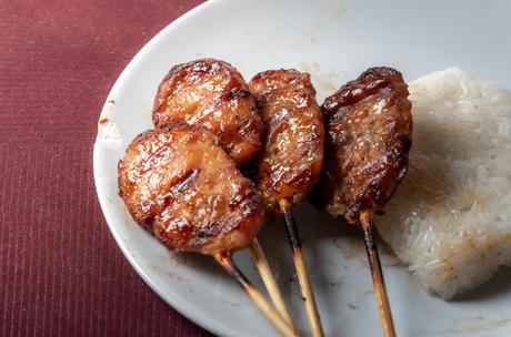 Gegrillte Fleischspieße mit Klebreis auf einem weißen Teller, auf einer roten Tischdecke.