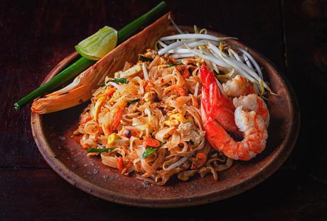 Ein Teller Pad Thai mit Garnelen, Sojasprossen, Limette und Garnitur als Beilage.