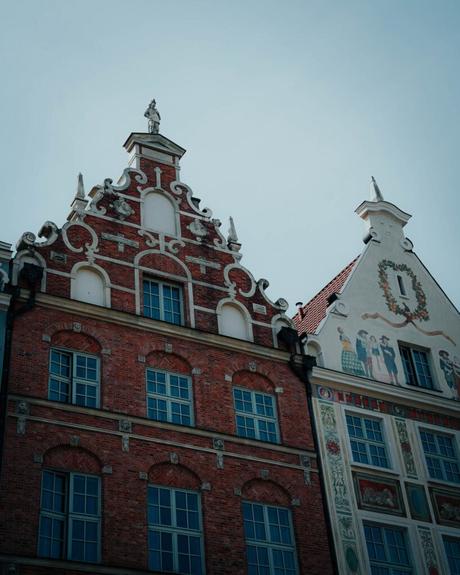 Zwei kunstvolle europäische Gebäude mit dekorativen Fassaden und großen Fenstern vor einem blassen Himmel.