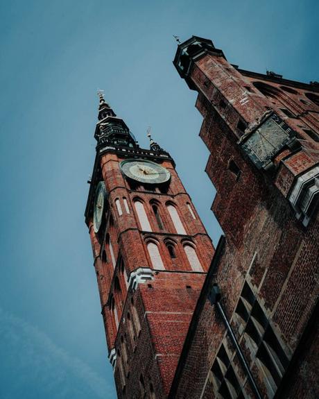 Ein hoher Uhrenturm aus Backstein mit einer Spitze vor einem blauen Himmel, aus einem niedrigen Winkel betrachtet.