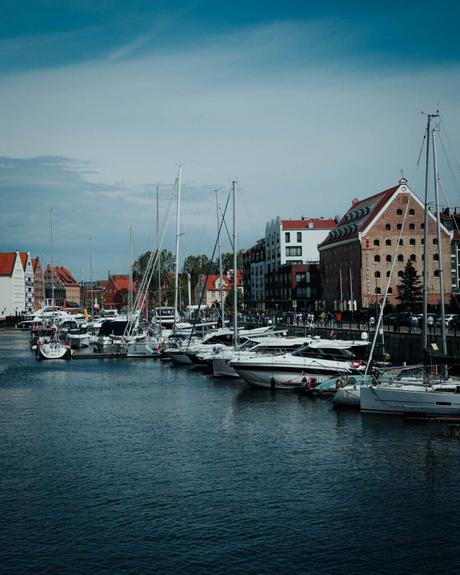 Yachten und Boote liegen in einem Yachthafen mit historischen Backsteingebäuden entlang der Uferpromenade.