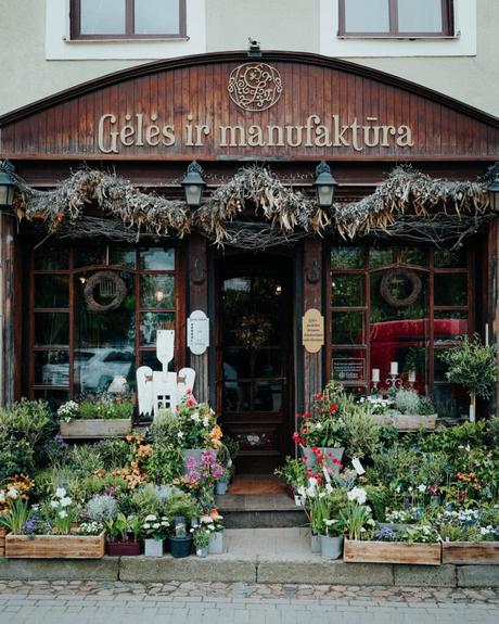 Außenansicht eines Blumenladens mit Holzdekor, Pflanzen und bunten Blumen vor dem Eingang.