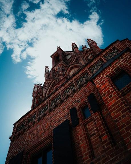Backsteingebäude im gotischen Stil mit verzierten Türmen vor einem blauen Himmel mit vereinzelten Wolken.